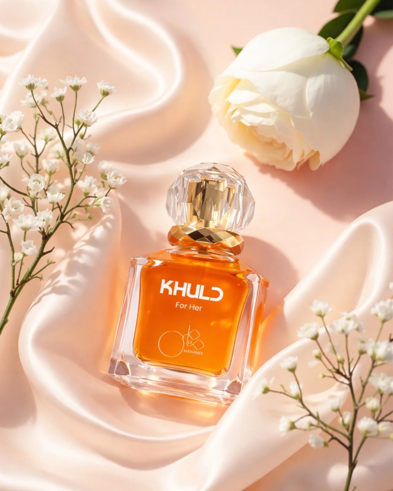 Orange perfume bottle labeled 'KHULD' on a soft pink background with white flowers.